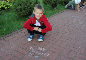 Filip prezentujący kropkowego misia, którego namalował na chodniku przed wejściem głównym do szkoły