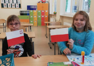 Weronika i Magda z klasy 1a prezentują przygotowane przez siebie flagi
